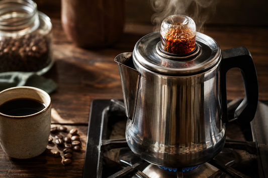 Stainless steel coffee percolator perking on a stovetop with coffee bubbling in the glass knob
