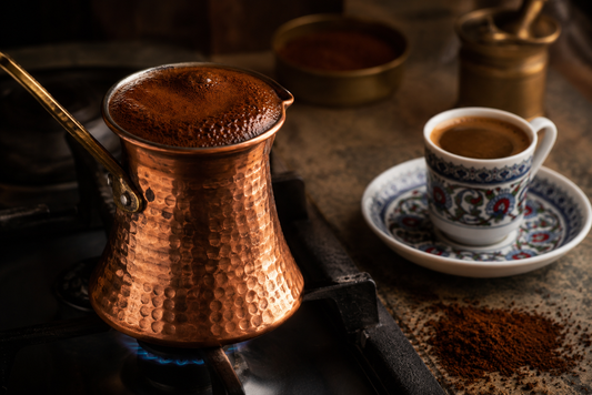 Copper Turkish coffee pot (cezve) brewing on a stovetop with foam rising to the neck