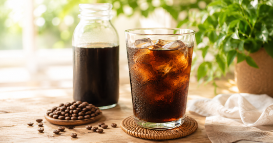 Glass of cold brew coffee over ice with concentrate jar and roasted beans