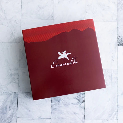 Deep red Hacienda La Esmeralda lid with white flower logo and Boquete mountain silhouette, top view on marble
