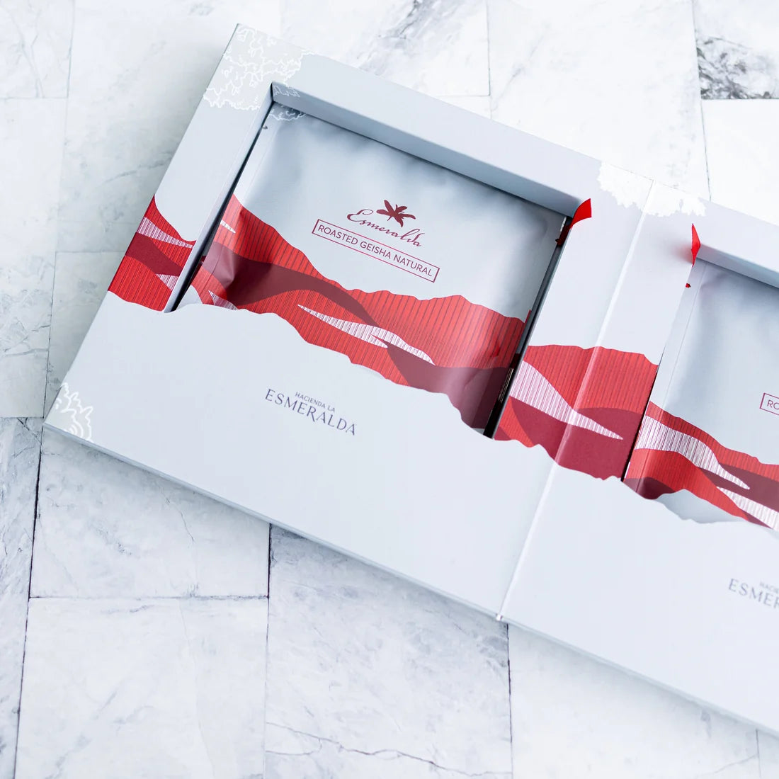 Open Hacienda La Esmeralda Geisha gift box showing sealed Roasted Geisha Natural coffee bags with red mountain design